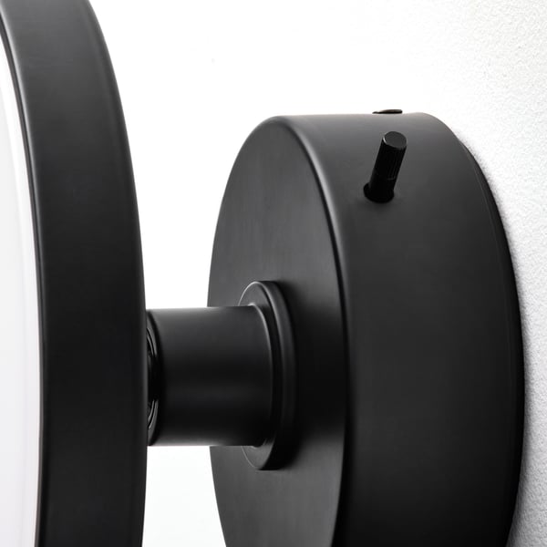 Black wall lamp with removable mirror, sleek design, mounted on light grey wall, modern art deco style.