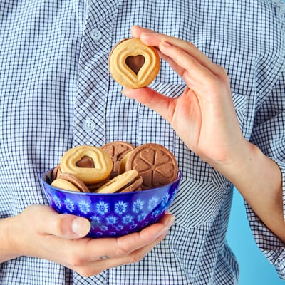 Person holding a blue bowl filled with heart-shaped cookies and a single heart-shaped cookie with a bite missing.