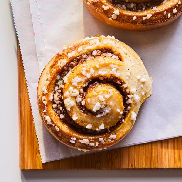 Two golden brown cinnamon rolls, spiral-shaped with sugar crystals, on parchment paper.