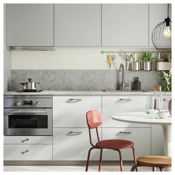 Modern kitchen with white cabinets, stainless steel oven, red chair, plants, hanging light, and metallic kitchen items.