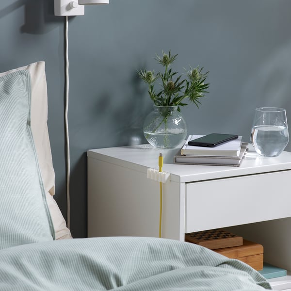 Bedside table with organised cables, using KALKSTUFF holders. White holders secure cables, keeping space tidy.