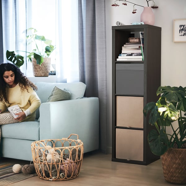 Person reading on light blue sofa near KALLAX shelving unit with baskets and books.