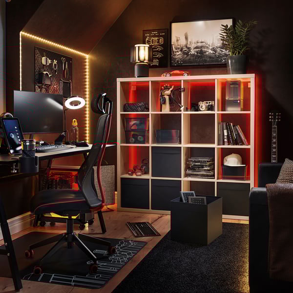 Home office with KALLAX shelf, red lights, guitar, desk, chair, monitor, keyboard, and plant.
