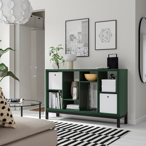 Green KALLAX shelf with books, boxes, plants, and pictures beside couch.