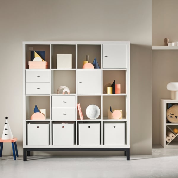 White KALLAX shelving unit with various coloured decor items. Modern, modular design with multiple compartments, drawers, and closed storage boxes.