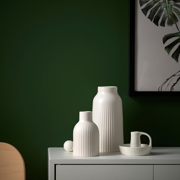 White stoneware vase with grooved design on table, green wall background.