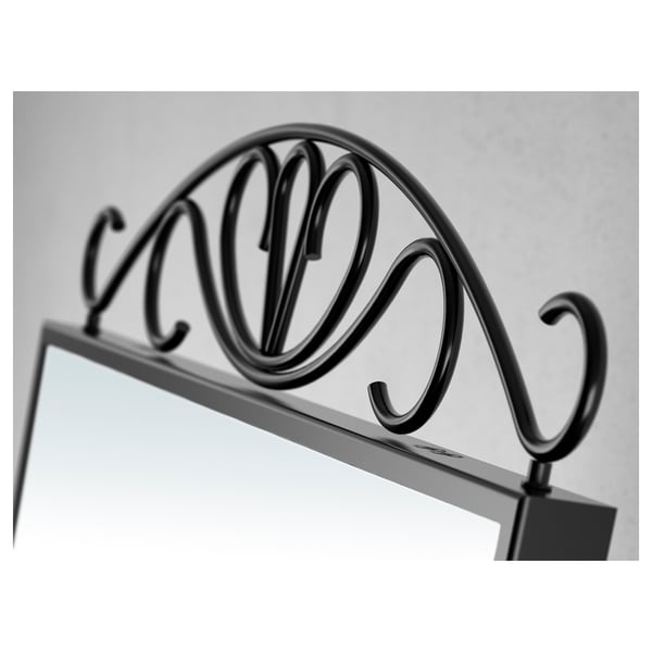 Black wrought iron mirror with ornate scrollwork detail at the top against a grey wall.