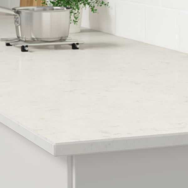 White quartz countertop with stainless pan, plant, and trivet. Durable, stain-resistant, easy to clean.