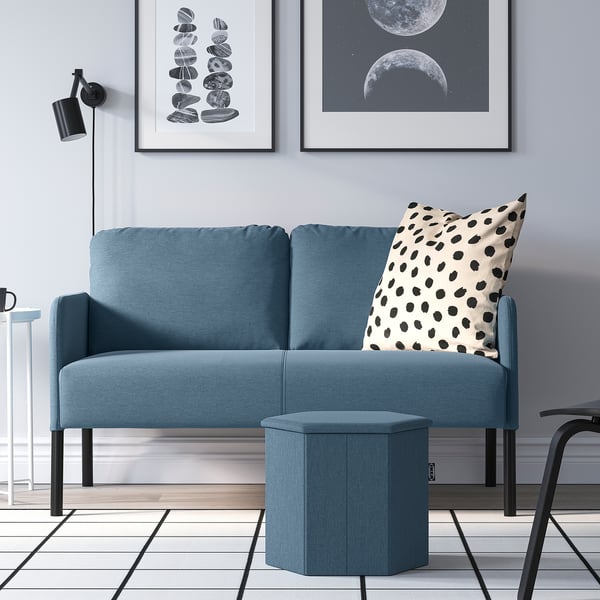 Modern living room with blue KJUGE sofa, polka dot pillow, round footstool, & art.