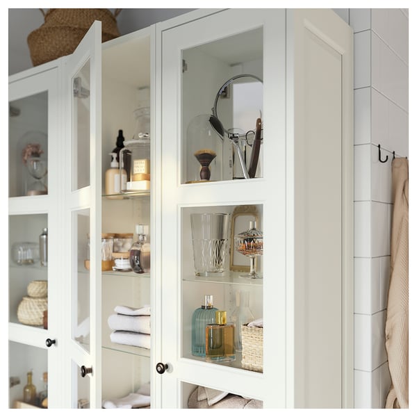 White cabinet with glass doors, showing neatly arranged items like jars, bottles, and towels.