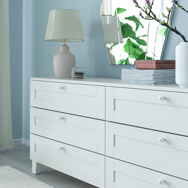 White dresser with 6 drawers and lamp, against blue walls.