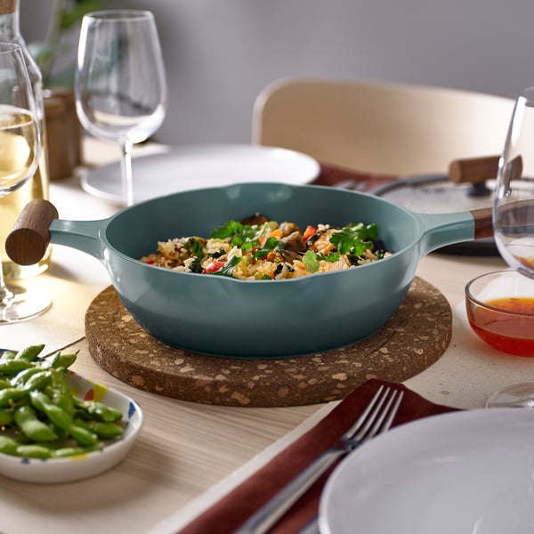 Dining table setup with teal KLIPPFISK sauté pan, colourful rice dish, glasses, forks, and place settings; rustic aesthetic.
