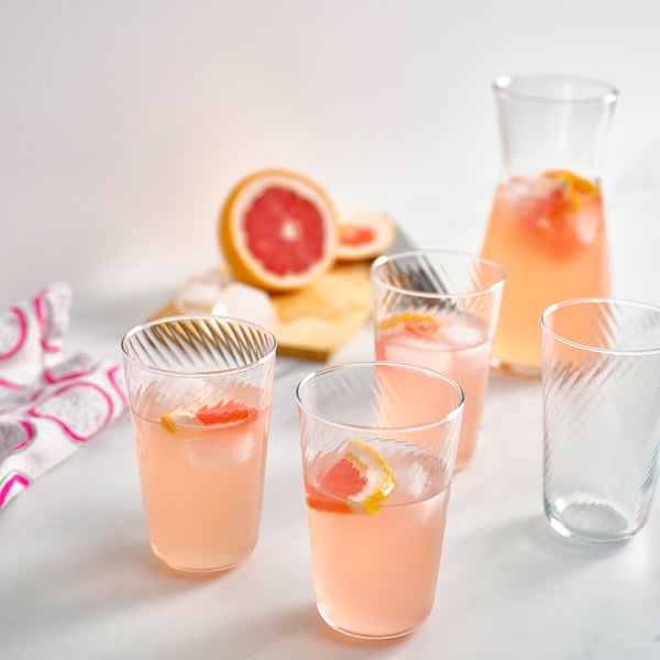 Four glass cups with pink grapefruit drinks, ice, and varying heights on a table.
