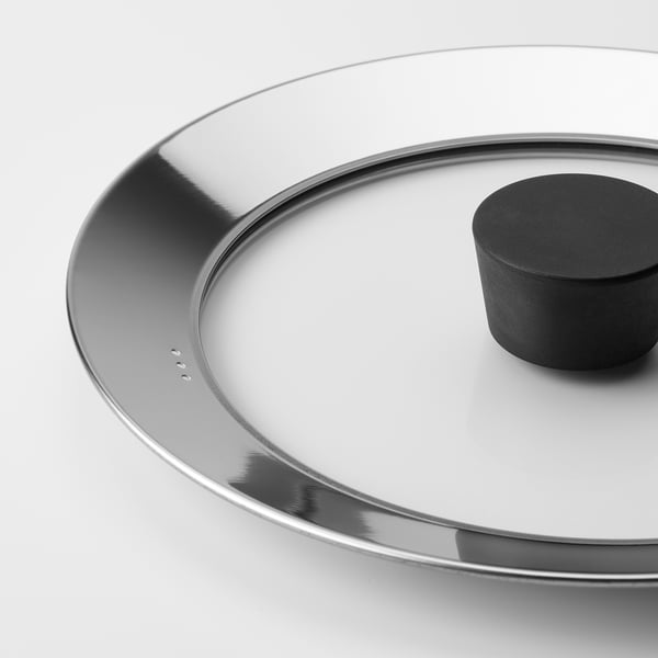 Close-up of KLOCKREN glass lid with metal rim, black handle, clean design.