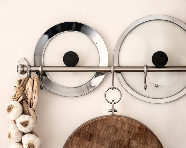 KLOCKREN silver lids hang on wall hooks with garlic bunch, wooden cutting board below.