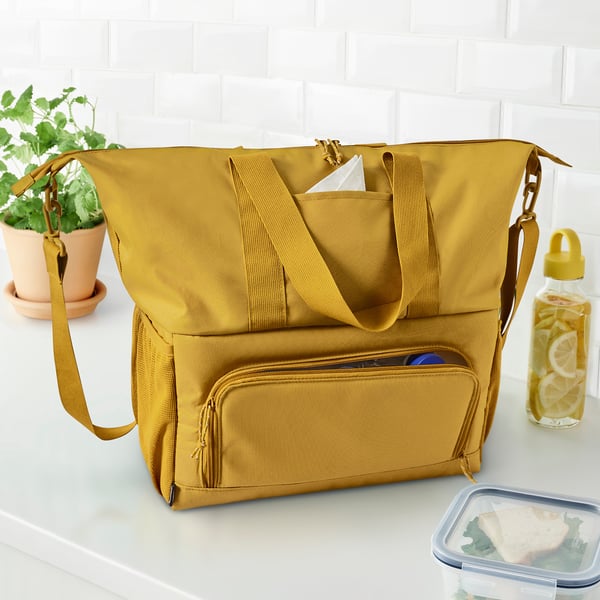 Large mustard-colored KLOTPIL insulated tote bag on table, surrounded by a plant, water bottle, and lunchbox.