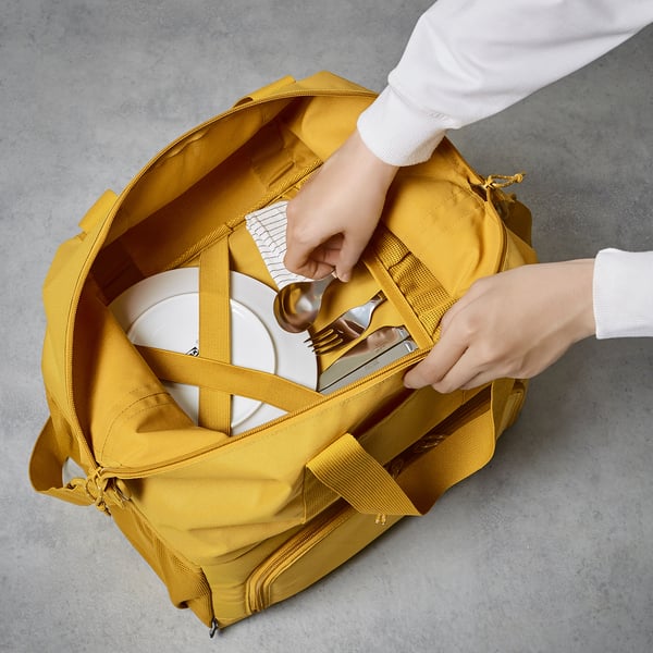 Person packing yellow KLOTPIL bag with insulated compartment and cutlery.