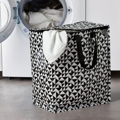 KNALLA black and white geometric laundry basket holds many items, positioned next to a larger white washing machine.