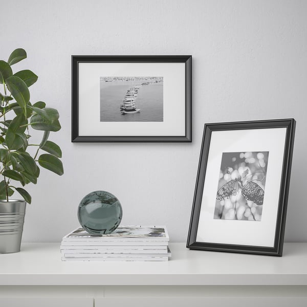 Black frames showcase sailboat and butterfly photos. Plant, books, sphere on white shelf.