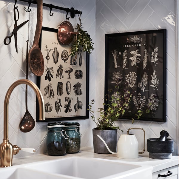 Modern kitchen decor: framed posters, hanging pots, potted plant, jars, sink, tap, mortar & pestle.