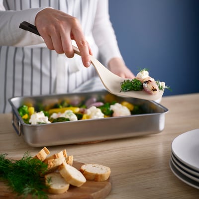 A person uses a spatula to serve food from a baking dish. The spatula has a wide blade and a sloped handle, making it easy to flip and serve.