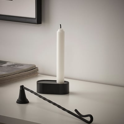 Black candle snuffer next to white candle in black holder on white surface.