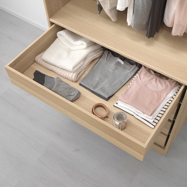 Open wooden drawer with neatly folded clothes and accessories, part of a pax wardrobe system.