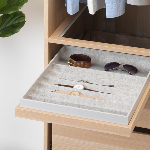 Open wooden drawer with felt tray shows watches, belt, and sunglasses, organised in compartments.