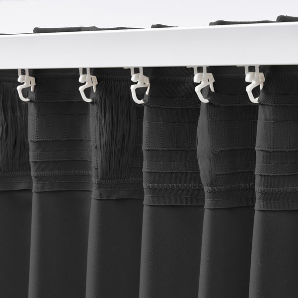 Black KORGMOTT block-out curtains with hooks hang neatly, offering light control and privacy. Curtains have eyelets for hanging.