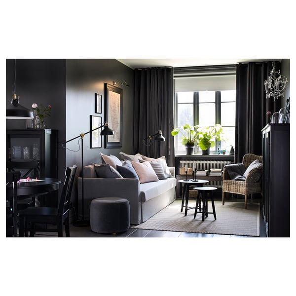 Modern living room with grey KRAGSTA nesting table, grey couch, wicker chair, dark curtains, and multiple decorative items, framed art, and plants.