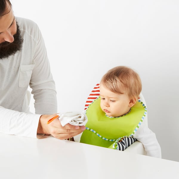 Person feeding baby with green bib using a washcloth.