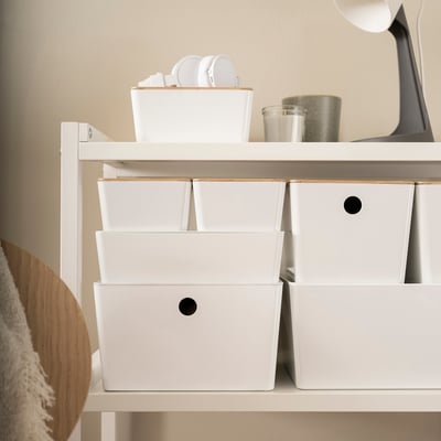 White KUGGIS storage boxes with bamboo lids, stacked neatly on shelves. Small, square, and lid-covered, fitting well with other home decor items.