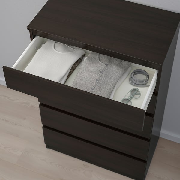 Dark wooden chest of drawers with one open drawer revealing neatly folded clothes and accessories.