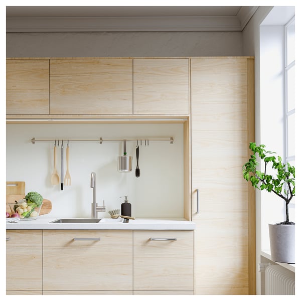 Modern kitchen with light wood cabinets, white countertops, and a metal rail holding kitchen tools.