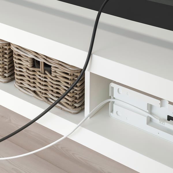 A white LACK tv bench with woven baskets and visible cable management behind.