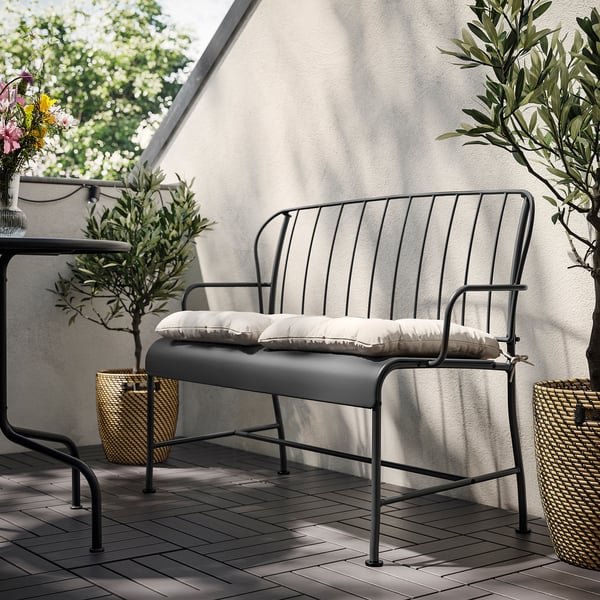 Modern outdoor black metal bench with white cushions against a light wall.