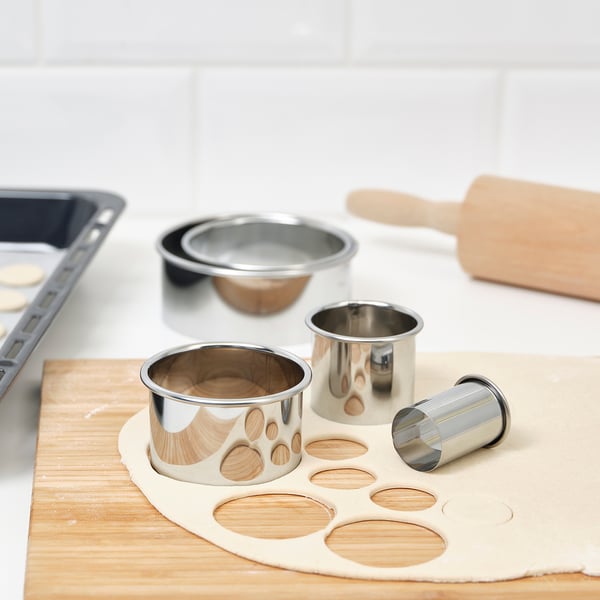 Metal cookie cutters in various sizes on dough. Includes rolling pin and tray, ideal for baking diverse cookie shapes.