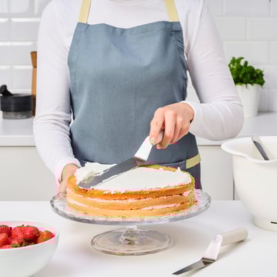A person is icing a cake with a spatula on a kitchen counter. A bowl of strawberries is nearby.