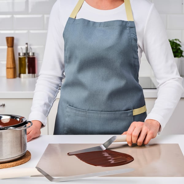 A chef uses an offset spatula to spread melted chocolate, demonstrating its use in baking.