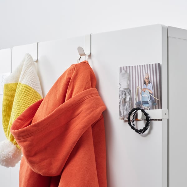 A white metal hook with orange cardigan hangs on a white door, beside a poster of a person ironing.