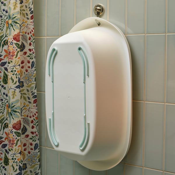 White baby bathtub with soft edges hangs on tiled wall, floral curtain nearby.