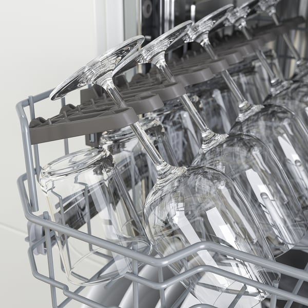 Clean dishes in a dishwasher, wine glasses securely held by prongs in the top rack, ensuring safe washing.