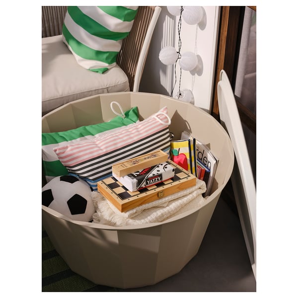 Large white storage bin filled with colourful items, placed in a cosy room with a striped pillow.