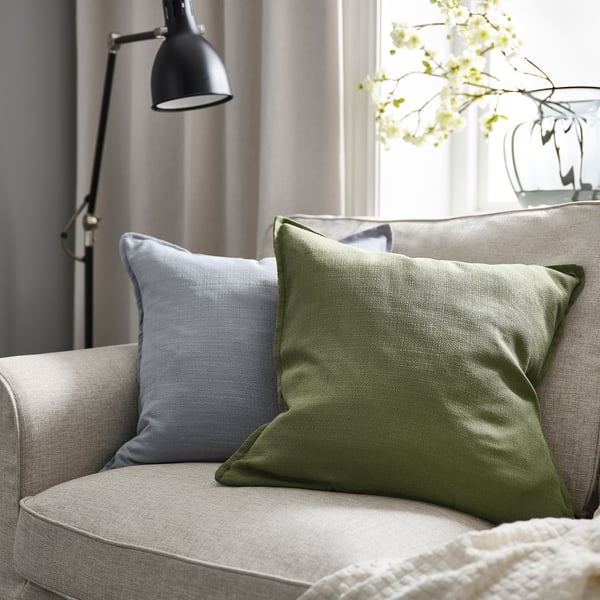 Cozy living room with grey-green cushion on beige sofa, blue pillow, lamp, and white flowers.