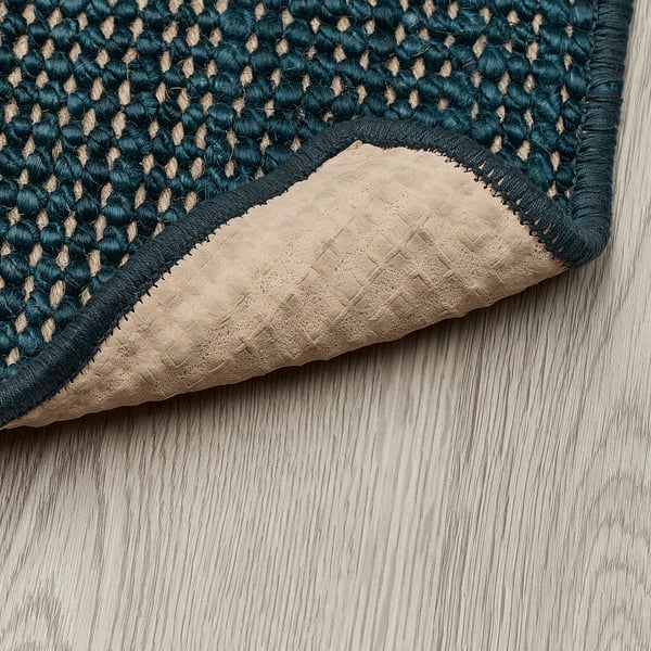 Dark blue jute door mat with natural latex backing sits on light wooden floor.