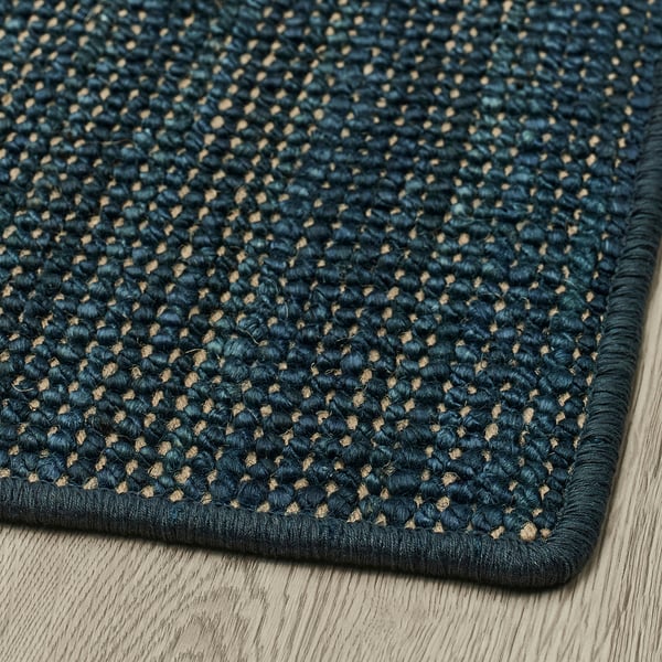 Dark blue textured woven rug with small dots on a wooden floor.
