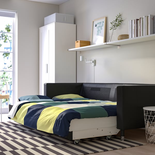 Modern bedroom with LANDSKRONA sofa-bed, striped rug, shelf with books and art.