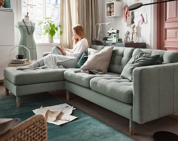 A cosy living room with a person reading on a grey LANDSKRONA sectional sofa with wooden legs.