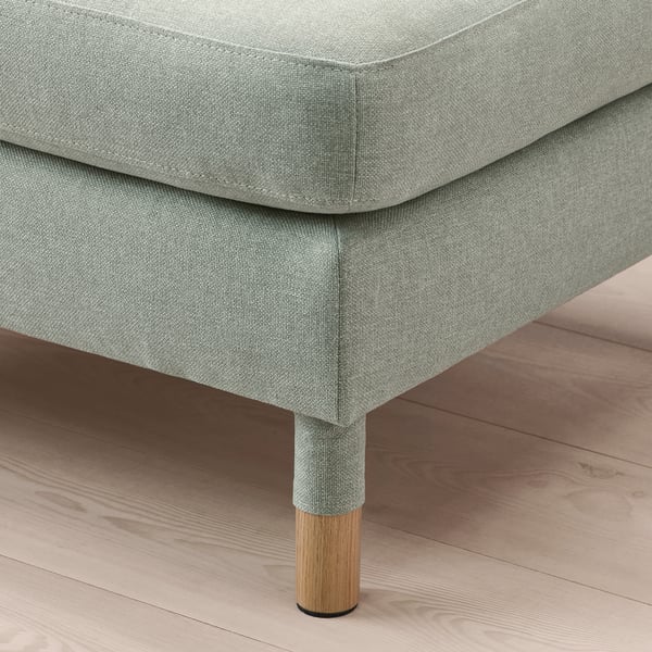 Close-up of stylish grey fabric-covered footstool with oak legs on wooden floor.