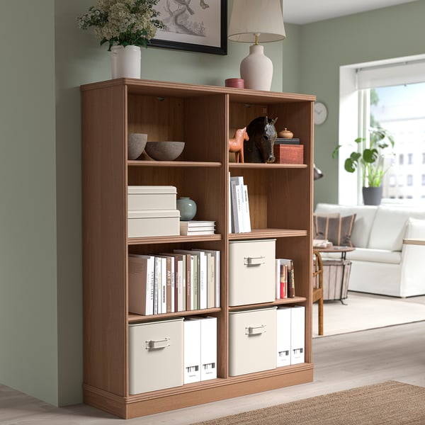 Light brown LANESUND bookcase with books, decor, and storage. Tall lamp and large painting above. Bright, open room with dining and sofa.